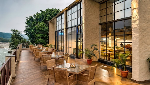 Un área de comedor al aire libre con mobiliario de mimbre y amplias ventanas con vistas a un río.