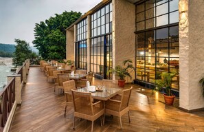 Un área de comedor al aire libre con mobiliario de mimbre y amplias ventanas con vistas a un río.