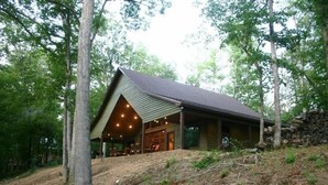 Eine moderne Hütte mit geneigtem Dach, großen Fenstern und einer überdachten Sitzgelegenheit im Freien.