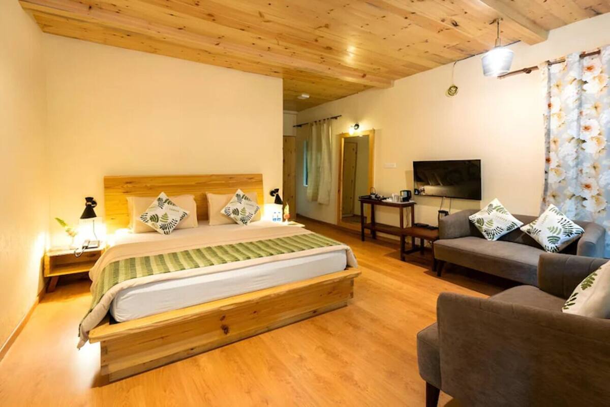 Een slaapkamer met een houten bed, een grijze bank, een televisie en een houten plafond.