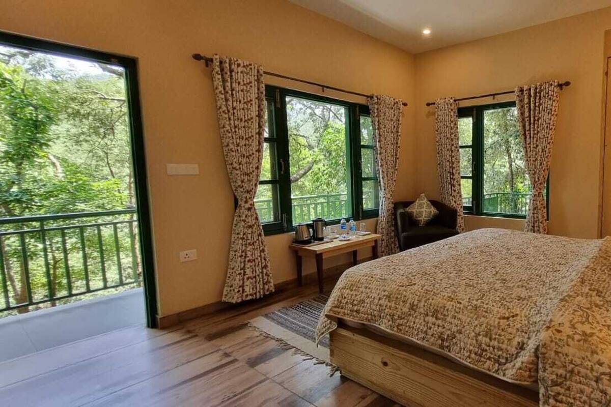 Een slaapkamer met een groot bed, twee ramen met gordijnen, een houten kledingkast en een klein tafeltje met een lamp.