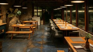 Restaurante com mesas e bancos de madeira, piso de ladrilho de pedra e luminárias pendentes.