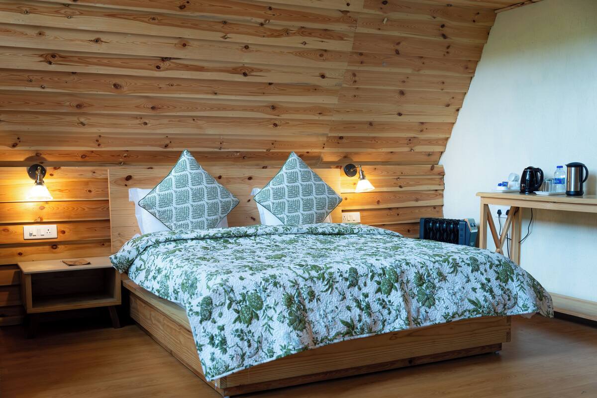 Een slaapkamer met houten lambrisering, een bed, twee nachtkastjes, een klein tafeltje met een waterkoker, en een wandlamp.