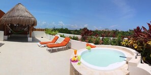 A rooftop pool area with lounge chairs, a hot tub, and a thatched-roof structure.