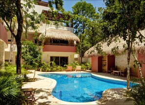 Un área de piscina con techo de paja, sillas de descanso y plantas tropicales.