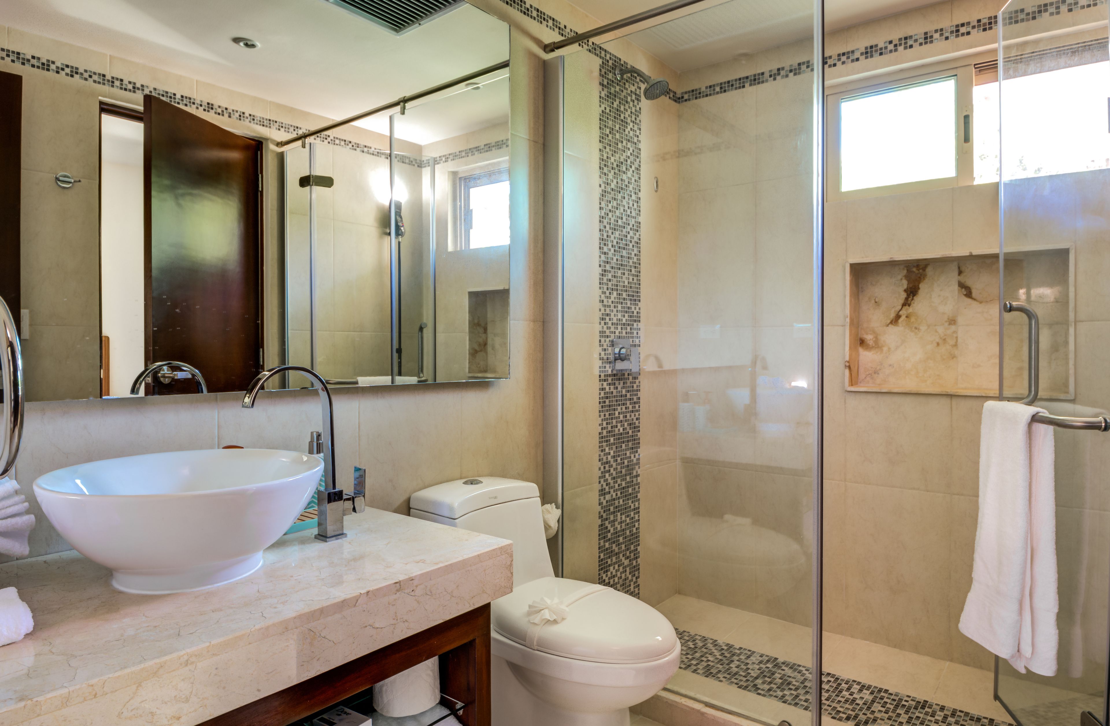 A modern bathroom with a large white sink, a glass-enclosed shower, and a marble-tiled shower wall.