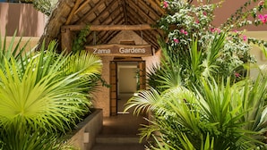 A thatched-roof entrance to Zama Gardens with a sign above the door.