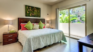 A bedroom with a large bed, two bedside tables, a nightstand, a window with a view of greenery, and a painting on the wall.