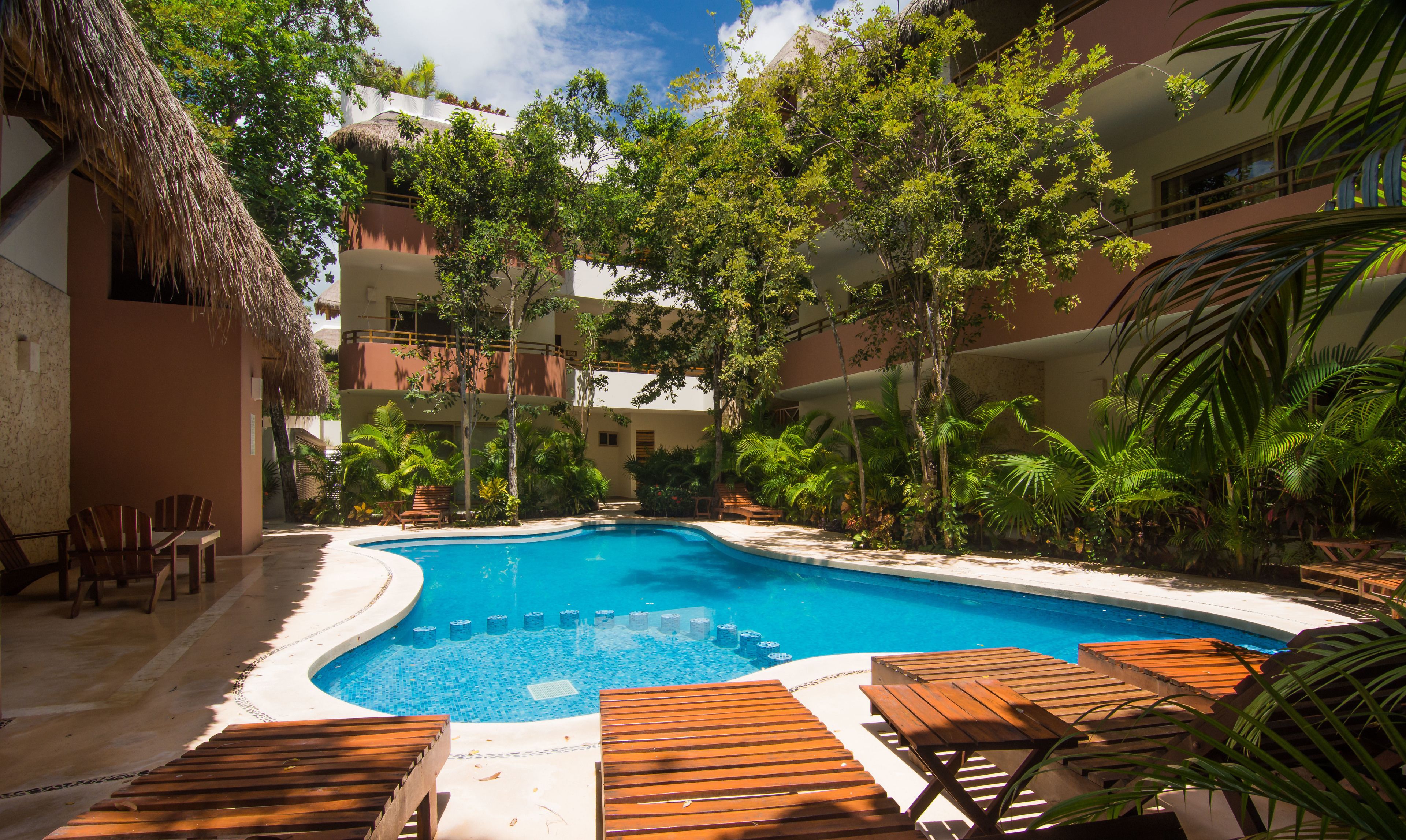 A swimming pool surrounded by wooden lounge chairs and tropical plants.