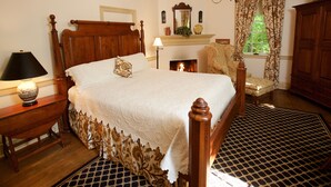 A traditional bedroom with a four-poster bed, a fireplace, a wooden cabinet, and a patterned rug. - The Zevely Inn (Winston-Salem)