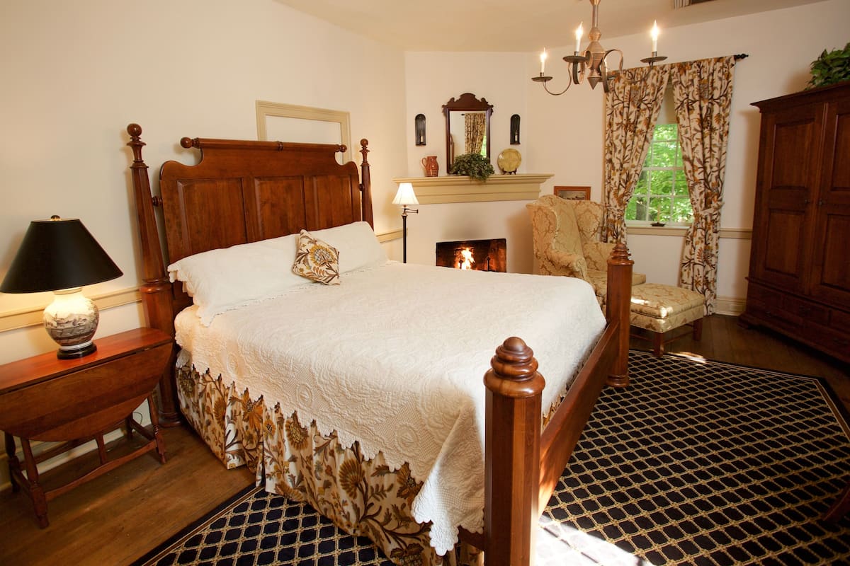 A traditional bedroom with a four-poster bed, a fireplace, a wooden cabinet, and a patterned rug.