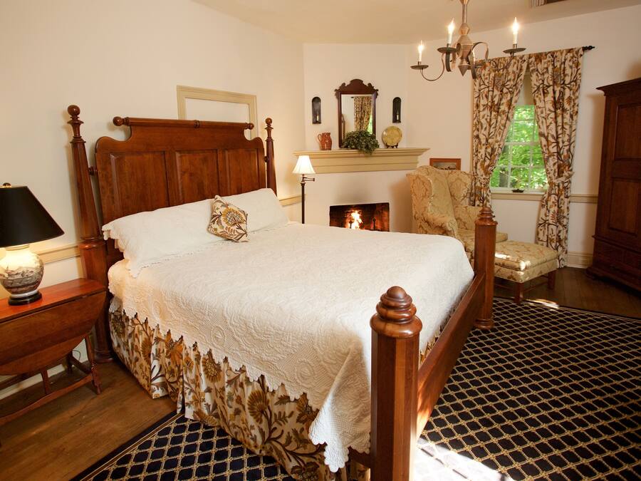 A traditional bedroom with a four-poster bed, a fireplace, a wooden cabinet, and a patterned rug.