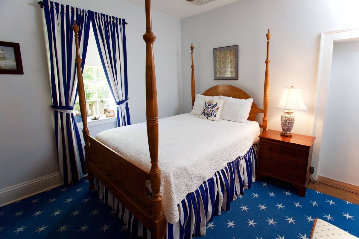 A four-poster bed with a white bedspread, a wooden headboard, and a nightstand with a lamp.