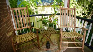 A wooden porch with two rocking chairs, a small table, and a potted plant. - The Zevely Inn (Winston-Salem)