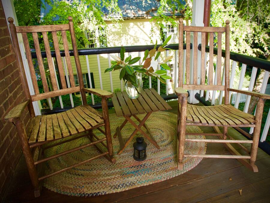 A wooden porch with two rocking chairs, a small table, and a potted plant.