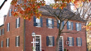 A red brick building with multiple windows and shutters, a street sign, and a lamp post. - The Zevely Inn (Winston-Salem)