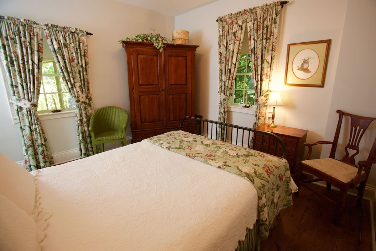 A bedroom with a bed, a wooden wardrobe, a chair, and a lamp.
