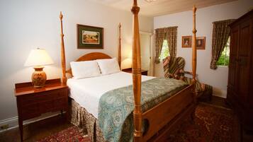 A four-poster bed with a wooden headboard, a bedside table with a lamp, a patterned rug, and a framed picture on the wall.