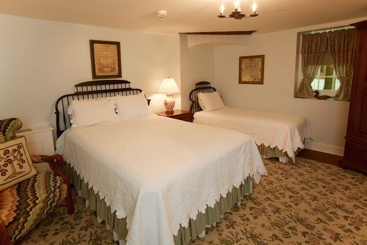 A room with two beds, a chair, a lamp, and framed pictures on the walls.