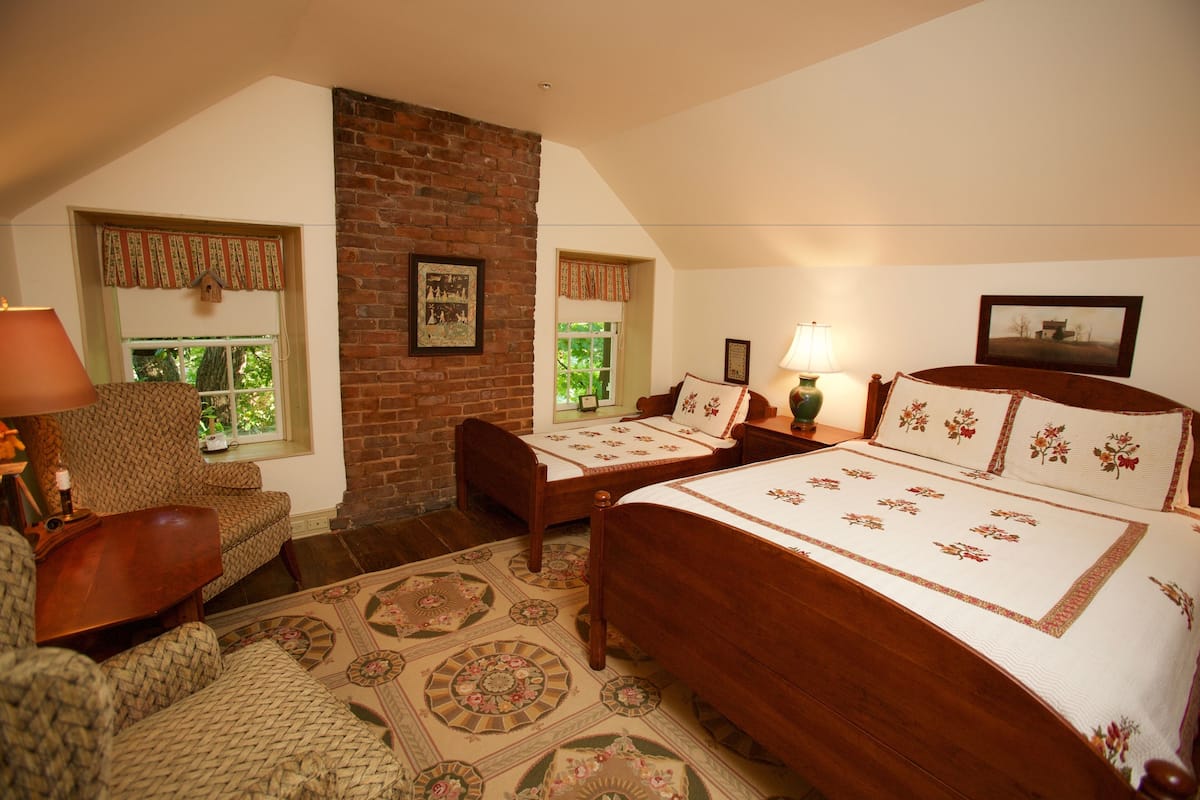 A bedroom with a large bed, two chairs, a wooden table, and a brick wall.