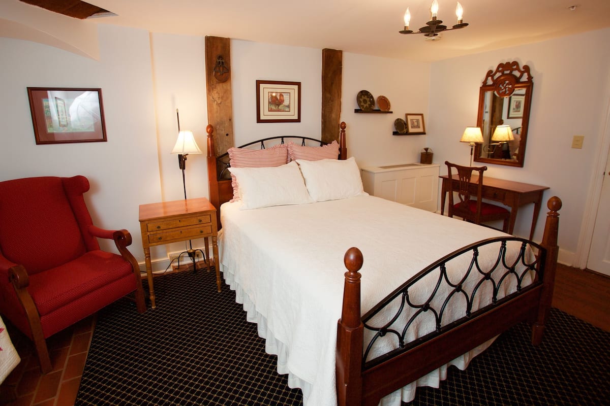 A bedroom with a bed, a chair, a nightstand, a lamp, a dresser, a mirror, and wall decorations.
