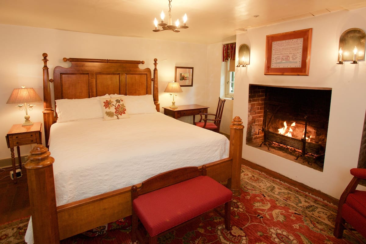 A traditional bedroom with a four-poster bed, a fireplace, and a red bench.