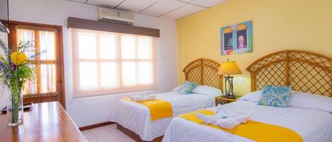 A hotel room with two beds, a wooden desk, a window with curtains, and a wall-mounted air conditioner.