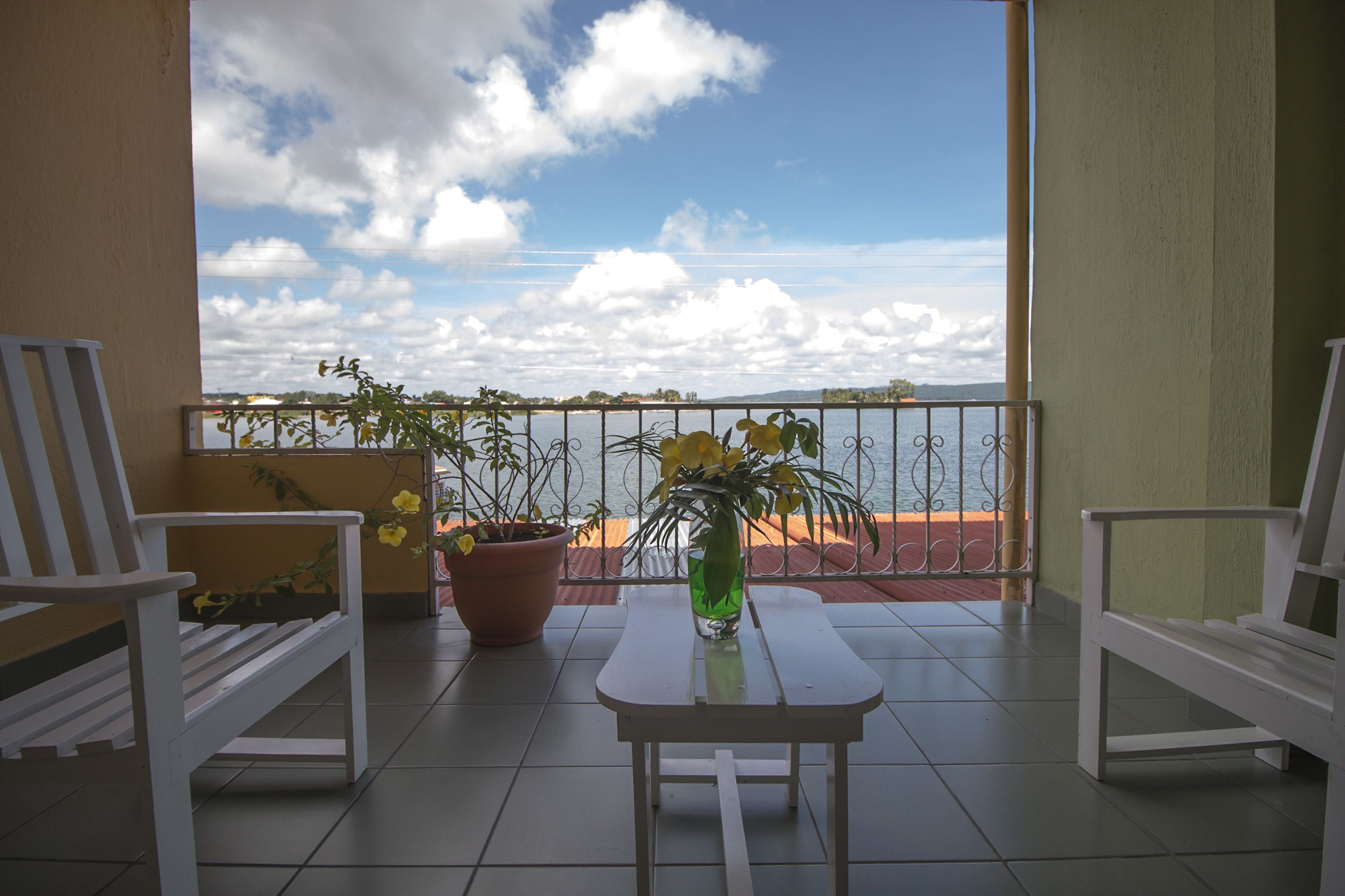 Ein Balkon mit zwei weißen Stühlen, einem kleinen Tisch und einem Blumentopf mit gelben Blüten.