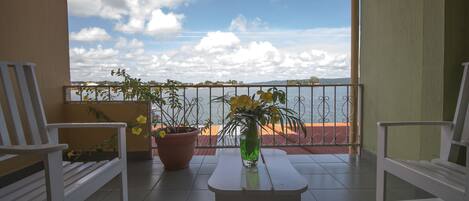 Ein Balkon mit zwei weißen Stühlen, einem kleinen Tisch und einem Blumentopf mit gelben Blüten.