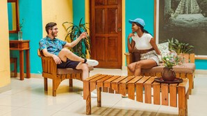 Um homem e uma mulher sentados em cadeiras de madeira num quarto com uma porta de madeira e o número '101' na parede.