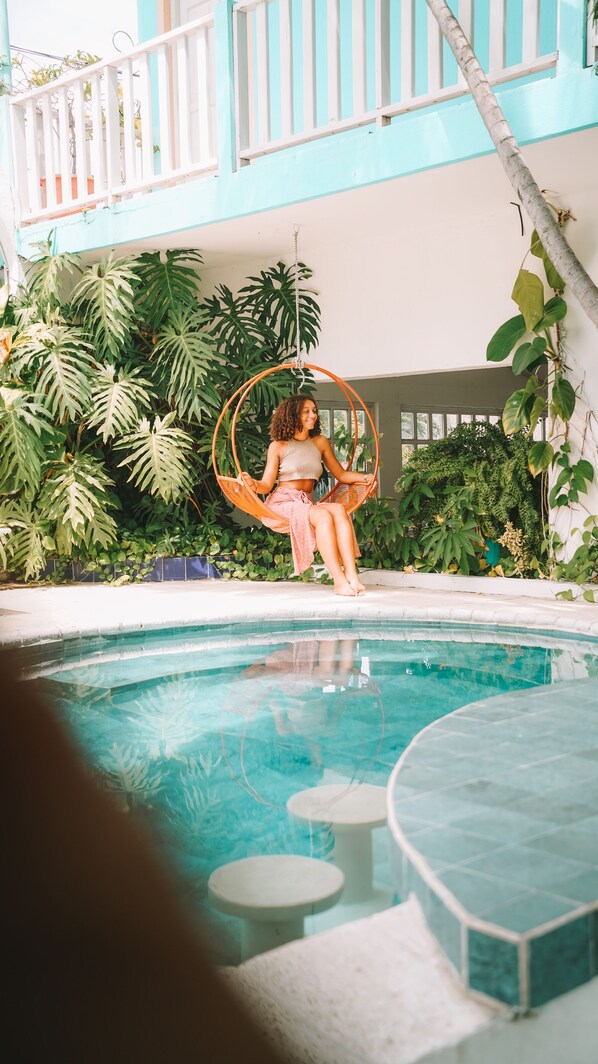 A person sitting on a swing chair by a pool with lush greenery in the background. - Hotel Santana (Flores)