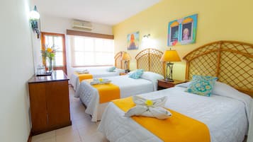 A hotel room with three beds, each with a yellow bedspread and white bedding. There are two wall-mounted lamps on each nightstand, and a wooden headboard with a lattice design.