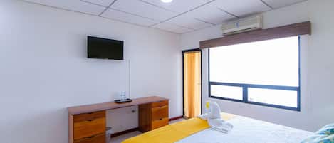Habitación de hotel con cama, escritorio con cajones, televisor de pantalla plana en la pared y ventana con cortinas.