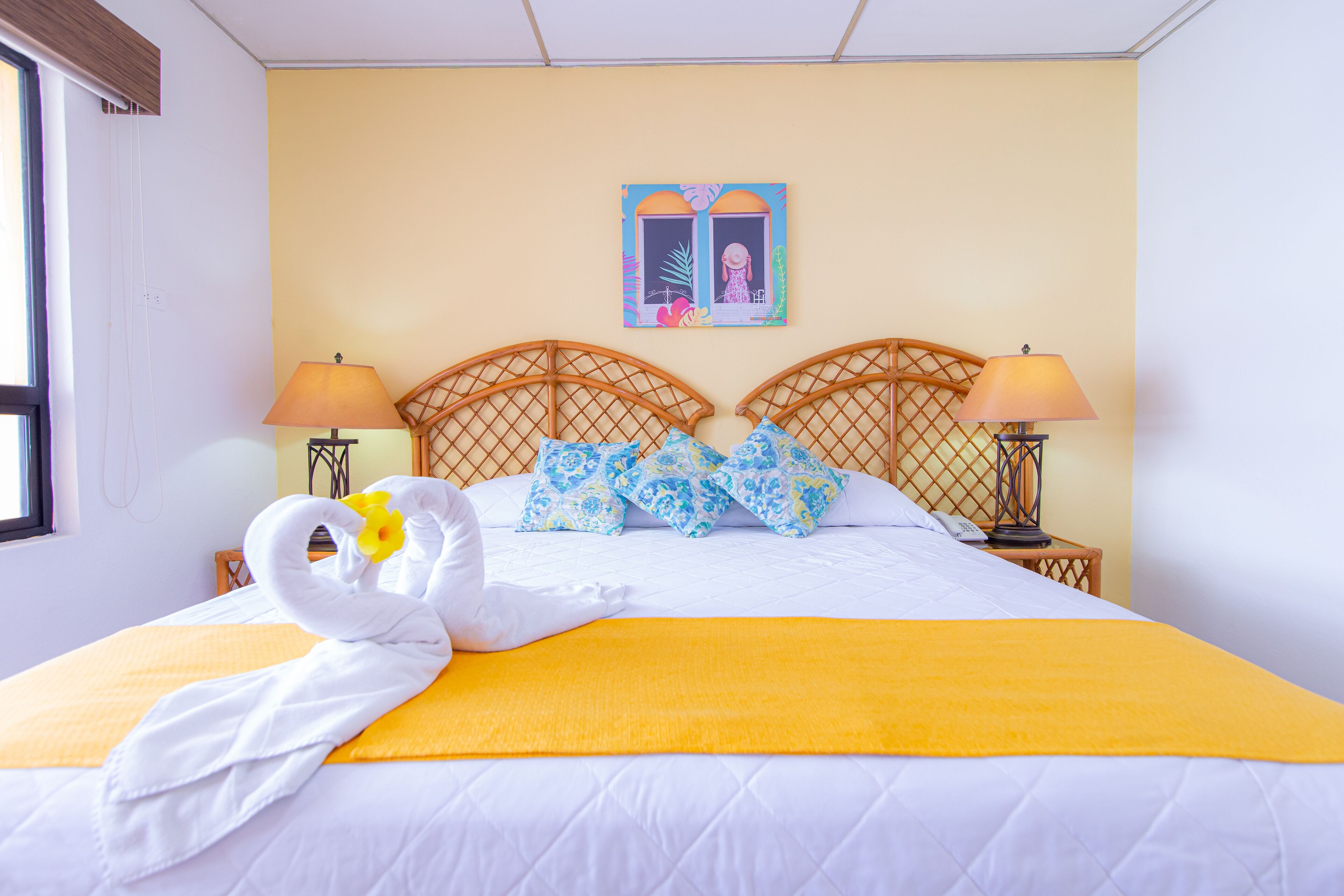 Una habitación de hotel con cama, dos lámparas de noche, una ventana y un cuadro en la pared.