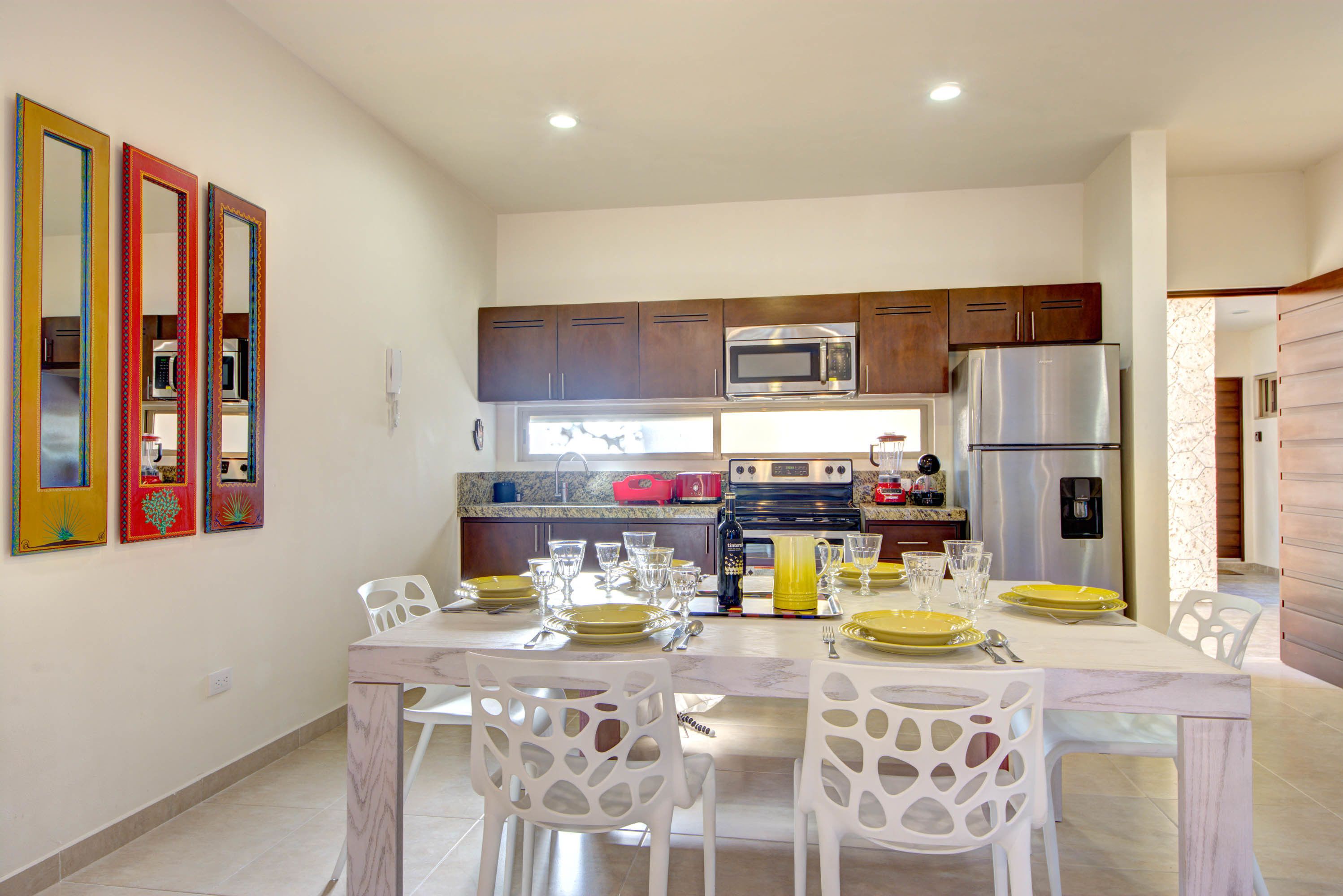 A modern kitchen with a dining area, featuring stainless steel appliances, white chairs, and a marble countertop.