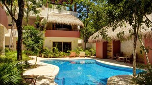 A pool area with a thatched roof, lounge chairs, and tropical plants. - Mijales 2 bedroom apartment sleeps 5 (Tulum)