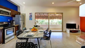 A modern kitchen with a microwave, stove, and refrigerator. There is a dining area with a table set for two, plates, and a fruit bowl. A TV is visible in the corner. - Rainbow Penthouse 2 bedrooms sleeps 5 (Tulum)