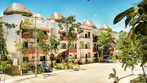 A resort with multiple buildings featuring thatched roofs, surrounded by lush greenery and a clear blue sky. - Rainbow Penthouse 2 bedrooms sleeps 5 (Tulum)