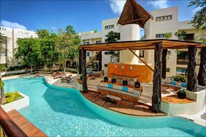 A swimming pool with a wooden deck and seating area, surrounded by buildings and trees. - Anita 2 bedroom apartment sleeps 5 (Tulum)