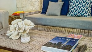 A modern living room with a stone wall, a grey sofa with blue and patterned cushions, a coffee table with decorative items, and a stack of magazines. - Villa Amore 4 bedroom house sleeps 8 (Tulum)