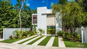 A modern house with a white exterior, a stone wall, and a well-maintained garden with a pathway leading to the entrance. - Villa Amore 4 bedroom house sleeps 8 (Tulum)