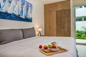 Una cama bien tendida con un carrito de desayuno, un cuadro de veleros y un armario de madera.