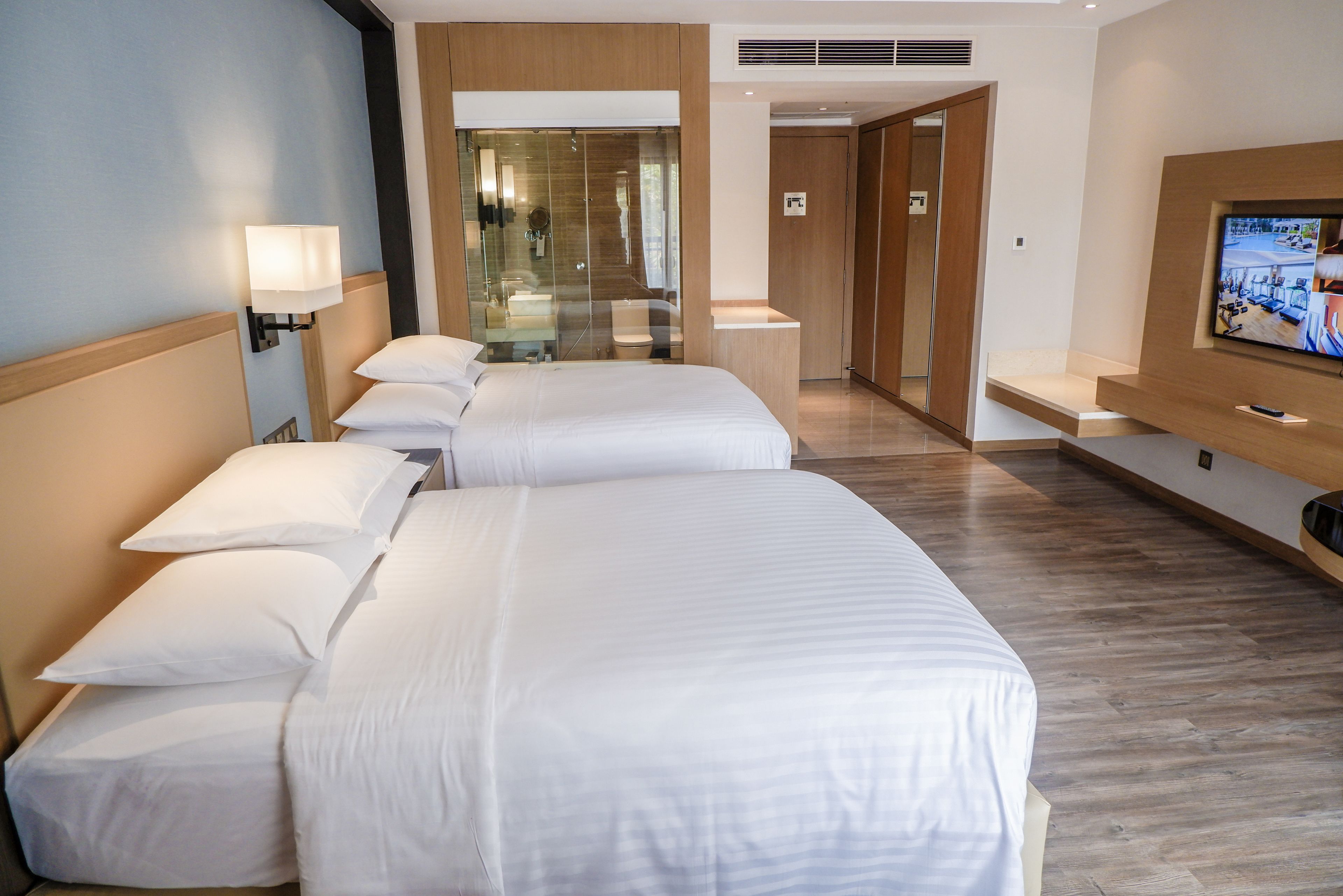 A hotel room with three beds, a TV, and a bathroom with a glass shower.