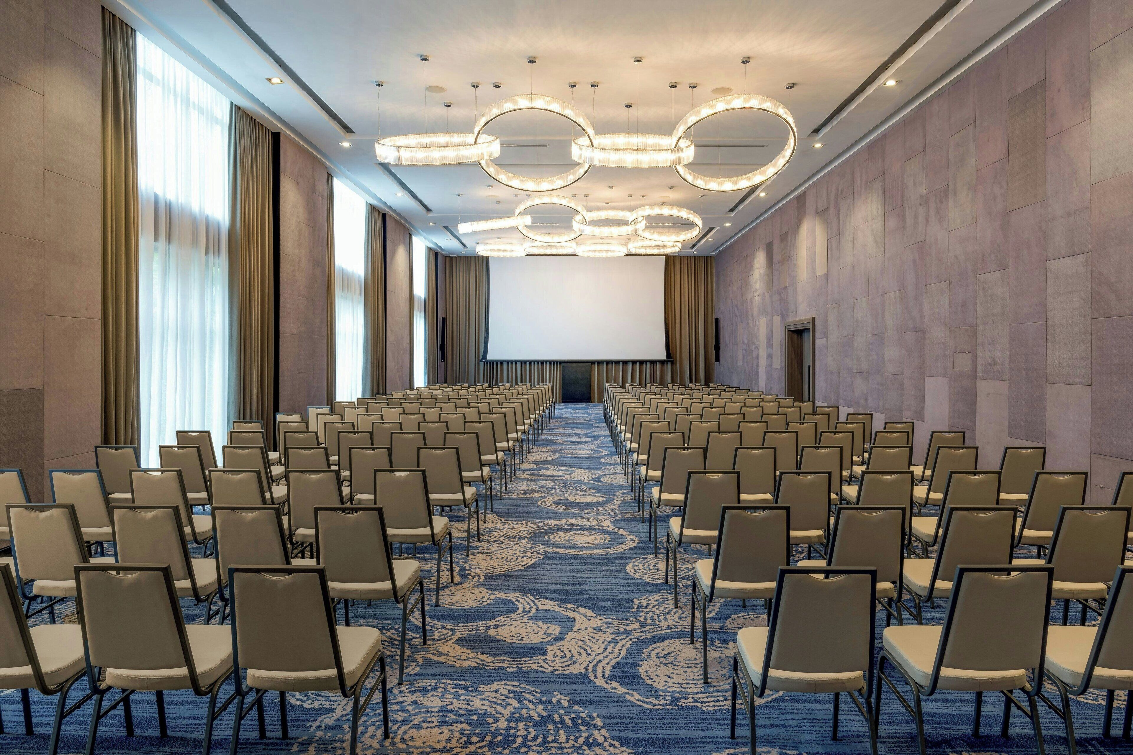 A conference room with rows of chairs, a large screen, and a patterned carpet.
