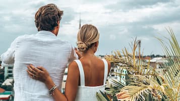 A couple standing on a balcony overlooking a cityscape with a cloudy sky.