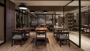 Un espace repas moderne doté de plusieurs tables et chaises, d’un plancher en bois et de luminaires suspendus.