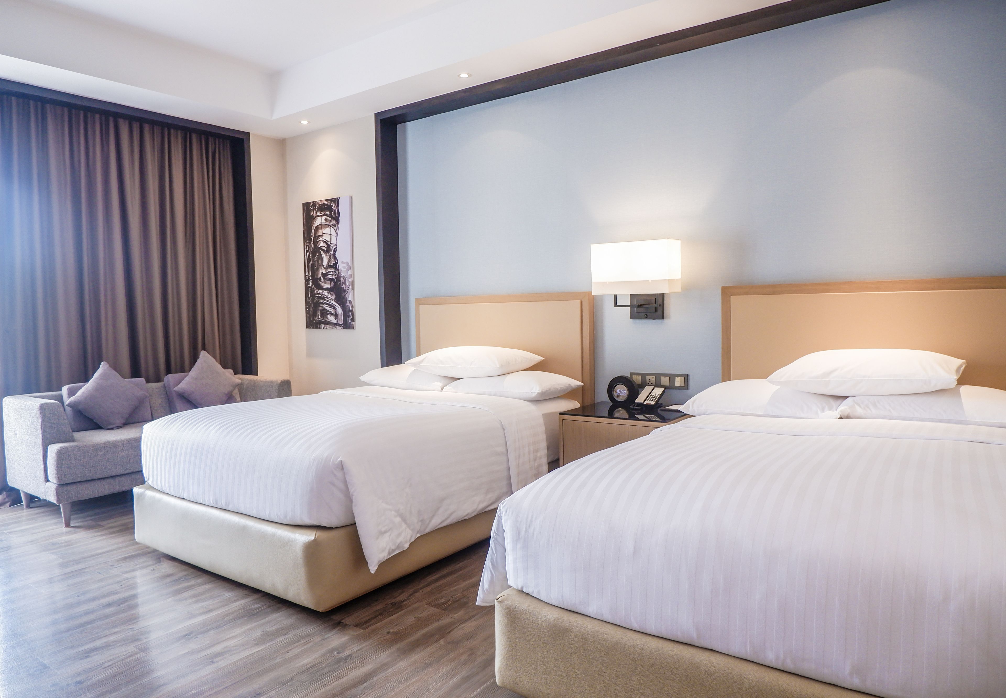 A hotel room with two beds, a sofa, and a nightstand with a lamp.