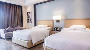 A hotel room with two beds, a sofa, and a nightstand with a lamp.