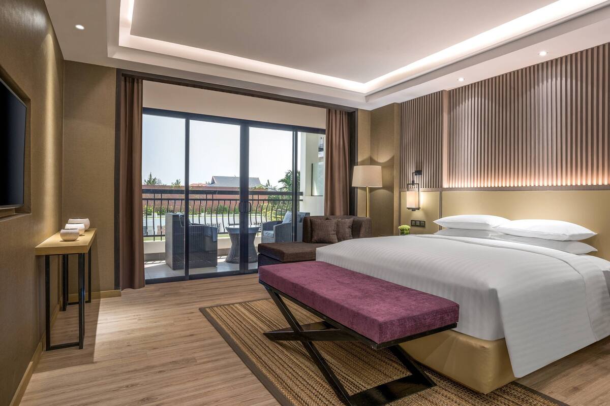 Une chambre d’hôtel moderne dotée d’un grand lit, d’une banquette, d’un bureau et d’un balcon aménagé avec du mobilier d’extérieur.