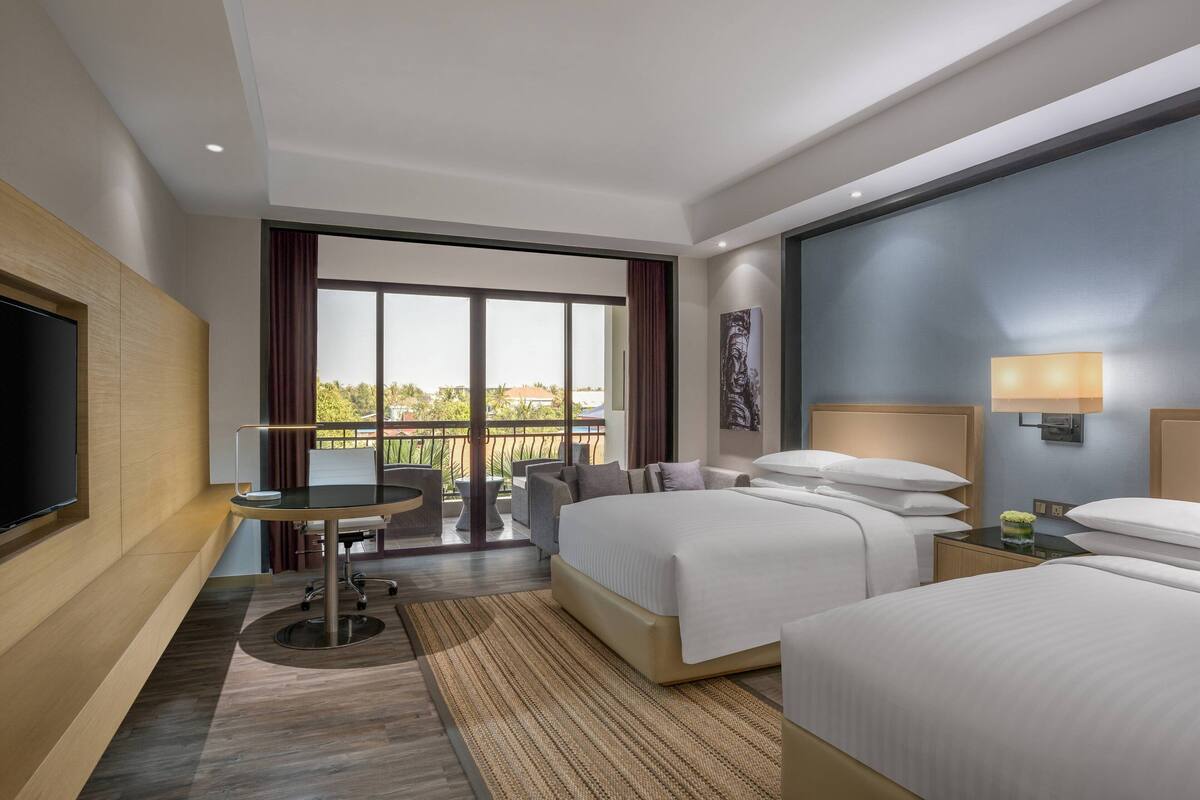 Une chambre d’hôtel avec un grand lit, un bureau et une télévision. Elle dispose d’un balcon avec vue sur l’extérieur.